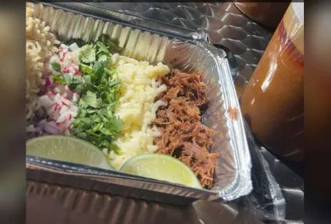 Catering tray of shredded birria, cheese, cilantro, radish and limes with consommé